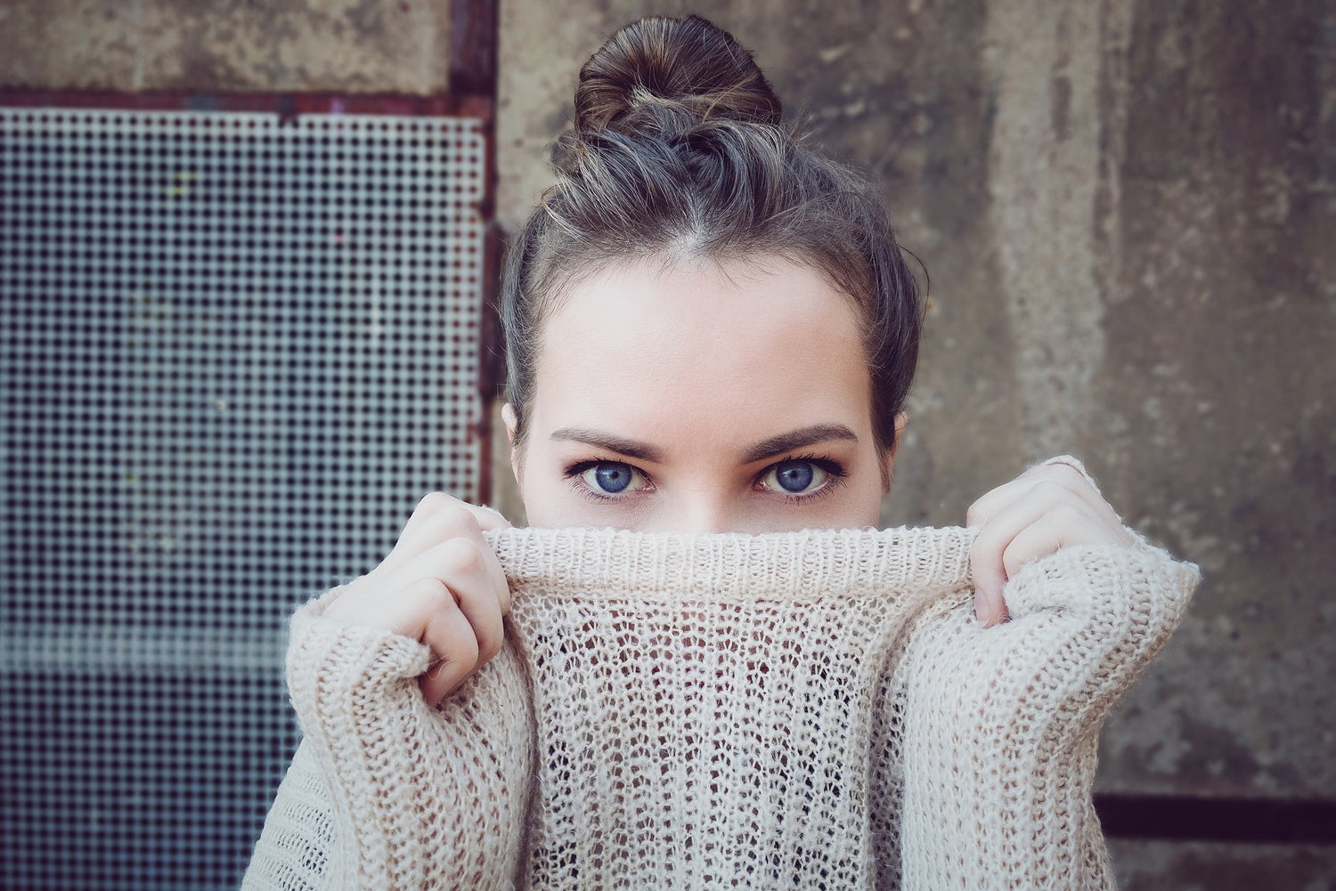 Woman holding the top of her sweater over her nose looking directly at you, like she is playing peek a boo